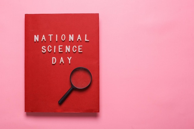 Flache Lage eines roten Buches mit der Aufschrift National Science Day isoliert auf rosa Hintergrund