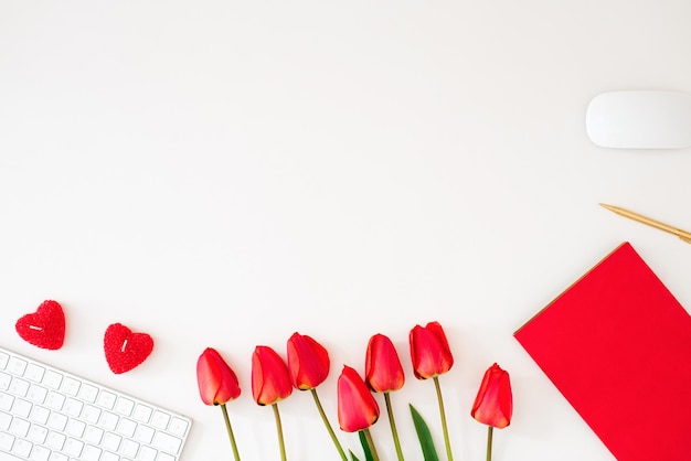 Flache Lage eines weiblichen Schreibtisches mit roten Blumen Frauenarbeitsplatz mit Tastaturtulpenzubehör