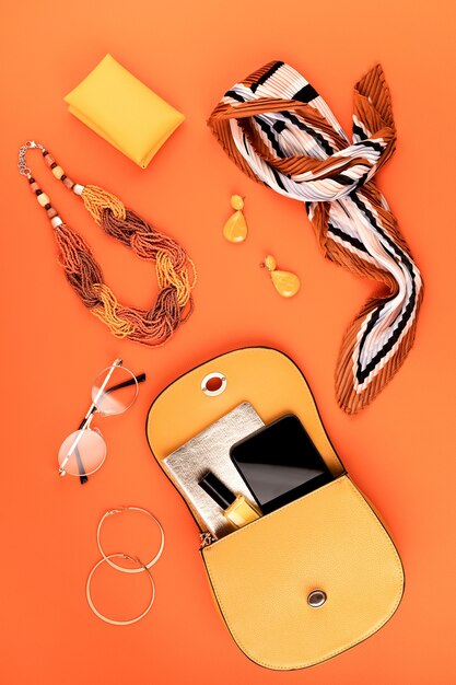 Flache Lage mit Damenmode-Accessoires in gelber Farbe über orange strukturierter Lederwand. Mode, Online Beauty Blog, Sommer Style, Shopping und Trends Konzept