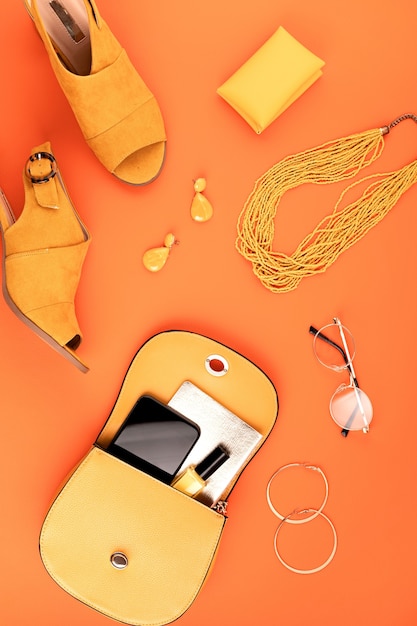 Flache Lage mit Damenmode-Accessoires in gelber Farbe über orange strukturierter Lederwand. Mode, Online Beauty Blog, Sommer Style, Shopping und Trends Konzept