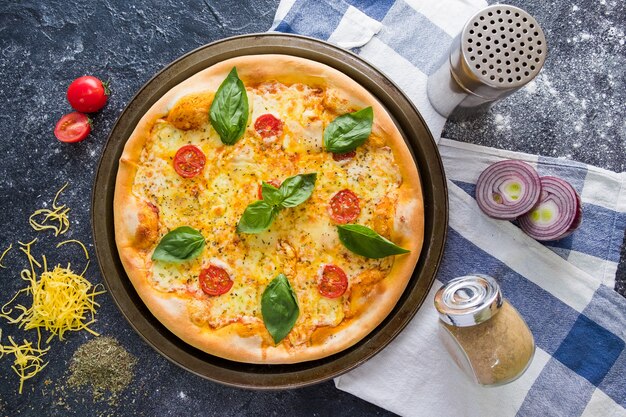 Flache lage mit traditioneller italienischer pizza mit tomaten, basilikum, mozzarella auf dunklem steintisch