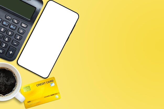 Flache Lage oder Draufsicht der Smartphone-Kaffeetasse-Kreditkarte mit Taschenrechner auf leuchtend gelbem Hintergrundtisch mit leerem Kopierbereich Mathematikkostensteuer oder Investitionsberechnung