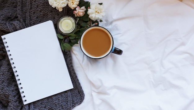 Flache Lage, Top-View-Home-Office-Traumarbeitsplatz mit Notebook, Kerze. Rosen, Kaffee auf dem Hintergrund von zerknittertem weißem Leinen und gestrickter grauer Tagesdecke, Raum bewältigen