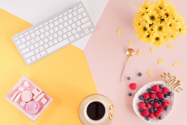 Flache Lage und Ansicht von oben genanntem des Arbeitsschreibtischs mit labtop Tastatur, Blumen und Beeren auf rosa und gelbem Hintergrund. Layout der weiblichen Pastelltabelle des Sommers