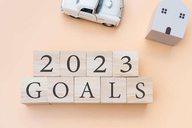 Flache Lage von 2023 Goals Brief auf Holzwürfel mit Modellhaus und Auto auf beigem Hintergrund Neujahrsplanung oder 2023 Zielkonzept Draufsicht