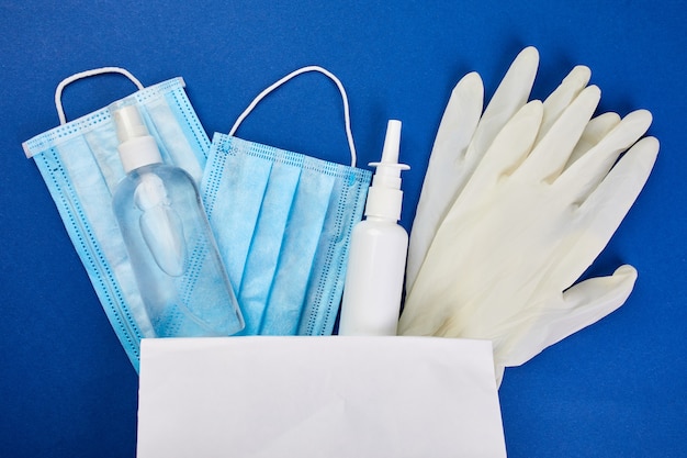 Flache Lage von Coronavirus-Schutz, medizinischen Schutzmasken, Handschuhen, Händedesinfektionsflaschen, Antiseptikum, Desinfektionsmittel, Spray in Einkaufstasche auf blauem Hintergrund, Kopierraum, Lebensmittelkonzept