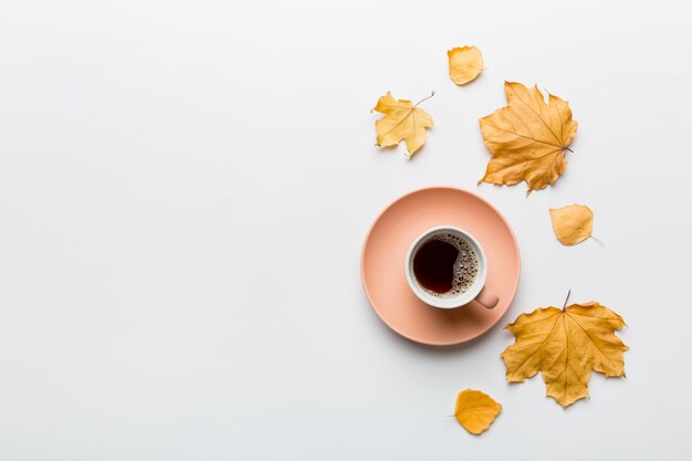 Flache Lagenkomposition mit bunter Herbsttasse Kaffee und Blättern auf einer Draufsicht des farbigen Hintergrundes