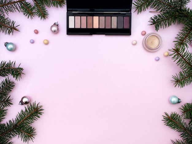 Flache Lagezusammensetzung mit kosmetischen Produkten des Make-ups und Weihnachtsdekor auf rosa Hintergrund