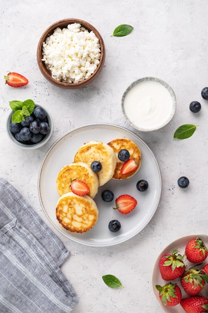 Flache Pfannkuchen mit Hüttenkäse mit frischen Blerries und Sauerrahm auf grauem Hintergrund Das Konzept eines gesunden und leckeren Morgenfrühstücks Draufsicht