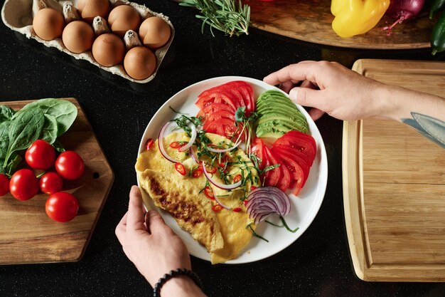 Flache Platte mit Omelett und Gemüse, die von männlichen Händen über ...