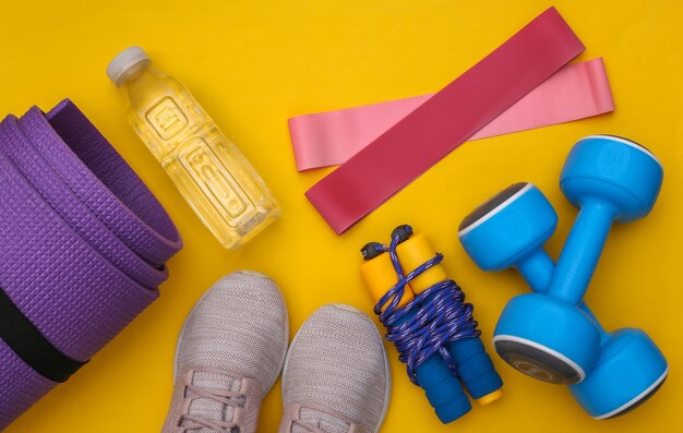 Flache Zusammensetzung von Fitness-Outfit, Zubehör auf gelbem Hintergrund. Gesunder Lebensstil, Sportkonzept. Ansicht von oben