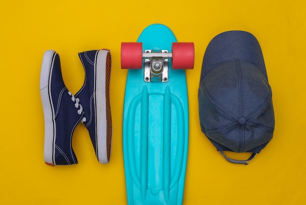 Flache Zusammensetzung von Mini-Cruiser-Board, Turnschuhen und Mütze auf gelbem Hintergrund. Jugend, Hipster-Accessoires. Ansicht von oben