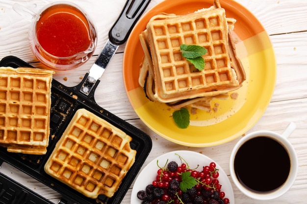 Flacher Blick auf belgische Waffeln auf gegossener Pfanne und gestapelt auf Teller mit Sirupbeeren und Kaffee