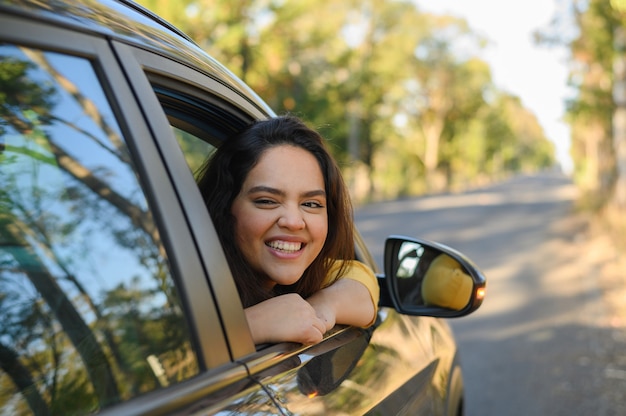 Flacher Fokus einer fröhlichen hispanischen Frau, die aus einem Autofenster auf der Straße schaut
