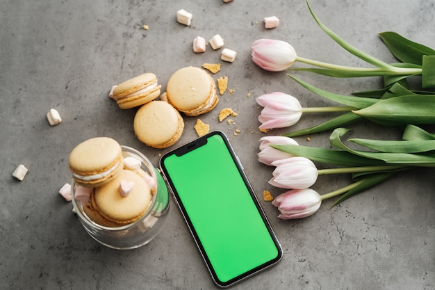 Flacher Hintergrund von frischen Tulpen, gelben französischen Macarons und Smartphone