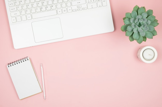 Flacher Home-Office-Schreibtisch. Frauenarbeitsplatz mit Laptop, Notizbuch, Stift auf rosa Oberfläche. Draufsicht weibliche Oberfläche.