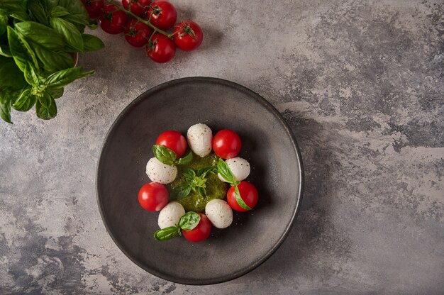 Flacher italienischer Caprese-Salat mit reifen Tomaten, frischem Basilikum und Mozzarella-Käse in schwarzer Platte