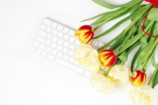 Flacher liegender Valentinstaghintergrund mit Computertastatur und Tulpenstrauß. Frühling Draufsicht.