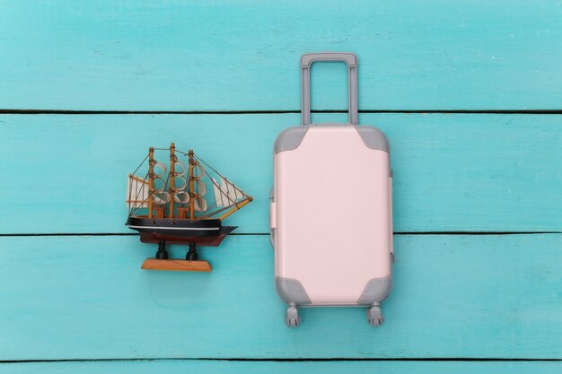 Flacher Urlaub Urlaub und Reiseplanung Konzept. Mini Reisekoffer aus Kunststoff und Schiff auf blauem Hintergrund aus Holz. Ansicht von oben
