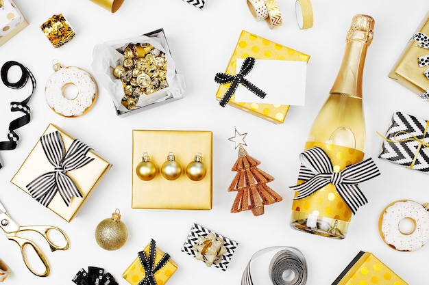 Flacher Weihnachts- oder Partyhintergrund mit Geschenkboxen, Champagnerflasche, Schleifen, Dekorationen und Geschenkpapier in den Farben Gold und Schwarz. Flache Lage, Ansicht von oben