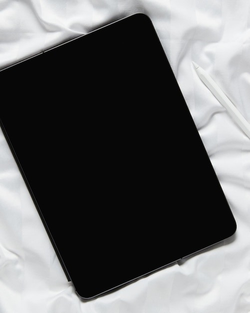 Flaches digitales Tablet mit Draufsicht und leerem Bildschirm auf weißem Bett im Home-Office-Arbeitsbereich