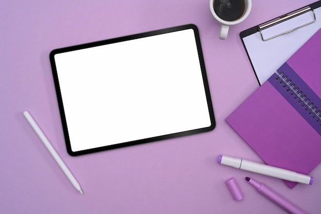 Flaches digitales Tablet mit leerer Kaffeetasse und Schreibwaren auf violettem Hintergrund