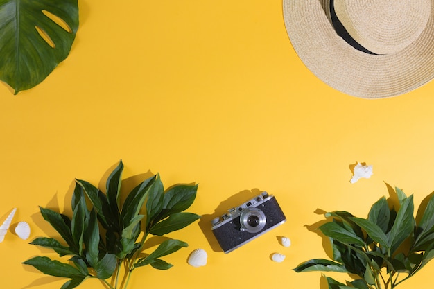 Flaches Lagendesign des gelben Hintergrundes mit Laptop, Fotokamera, tropischem Blatt der grünen Palme und Blumen, Draufsicht. Sommerhintergrund, Ferien und Feiertage, Reise- und Reiseplanungskonzept