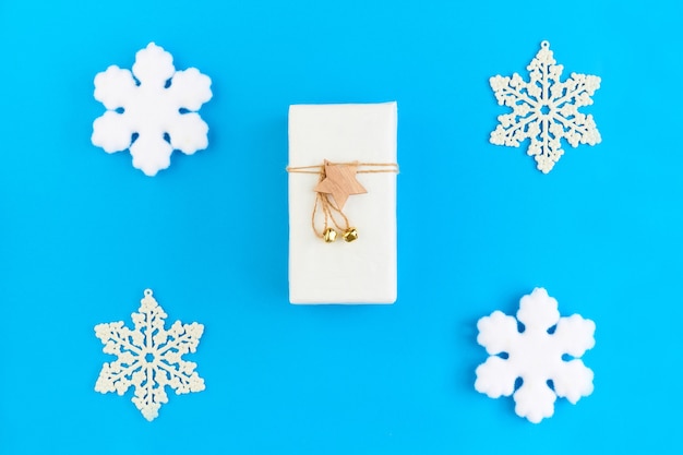 Flaches Layout des weißen Pakets mit Weihnachtsgeschenk mit Holzstern und Faden oben, umgeben von einer Gruppe von Schneeflocken auf blauem Hintergrund