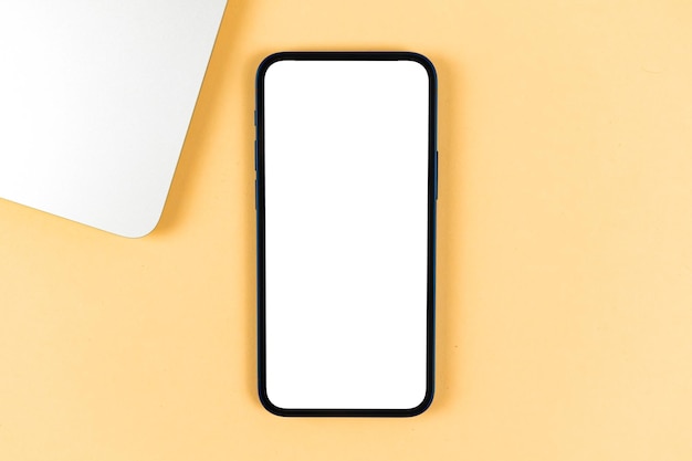 Flaches Smartphone-Modell, Büro-Desktop mit Laptop, hellbeiger Hintergrund. Ansicht von oben, Platzfoto kopieren