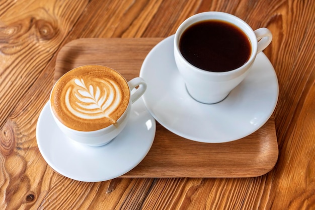 Flaches Weiß oder Cappuccino und Filterkaffee in weißen Tassen auf Holztisch Verschiedene Kaffeestile Morgengetränk im Café auf kleinem Holztablett