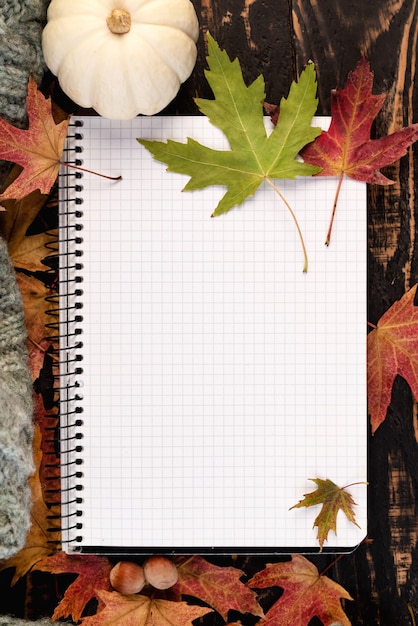 Flaches weißes Notizbuch mit Eicheln und Herbstlaub auf Holztisch. Herbststillleben. Gemütliche Herbststimmung. Platz kopieren.