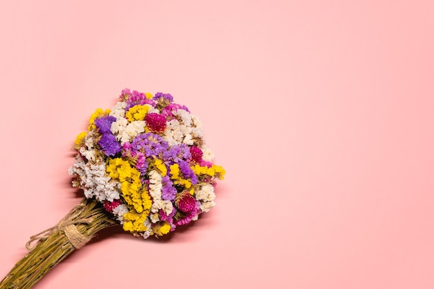 Flachfoto mit einem vielfarbigen Blumenstrauß mit getrockneten Blumen Limonium auf pastellrosa Hintergrund