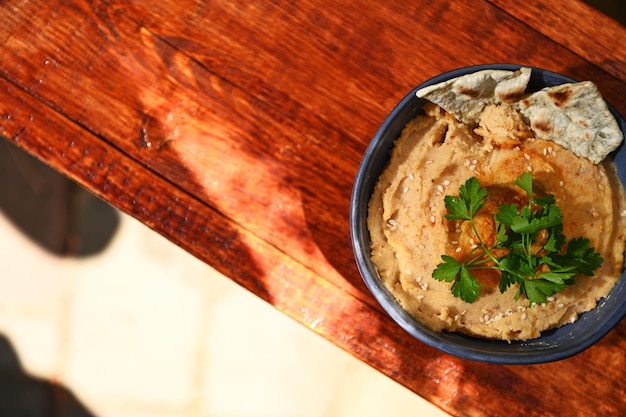 Flachgelegter Kichererbsen-Hummus-Dip mit Fladenbrot auf einer blauen Keramikschale auf Holzhintergrund mit Werbefläche für Text