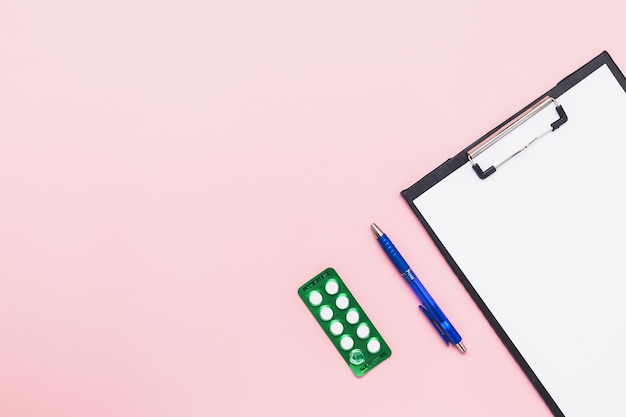 Foto flachgeschicht mit papier, blauem stift und blisterverpackung mit medikamentenpillen auf rosa hintergrund