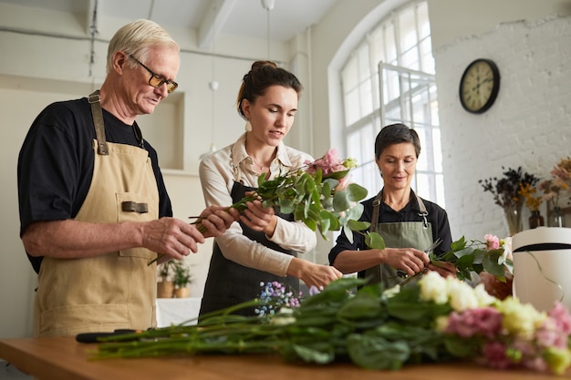 Flachwinkelporträt von drei kreativen Floristen, die in der Werkstatt Blumenkompositionen anordnen