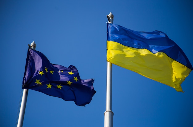 Flagge der Europäischen Union und ukrainische Flagge, die gegen blauen Himmel flattern