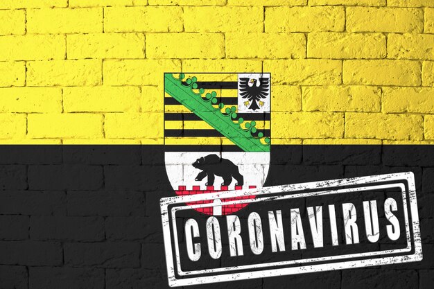 Flagge der Regionen Deutschlands Sachsen-Anhalt mit Originalproportionen. gestempelt mit Coronavirus. Mauer Textur. Konzept des Corona-Virus. Am Rande einer COVID-19- oder 2019-nCoV-Pandemie.