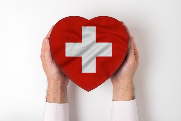 Flagge der Schweiz auf einem Herzen formte Kasten in männliche Hände.