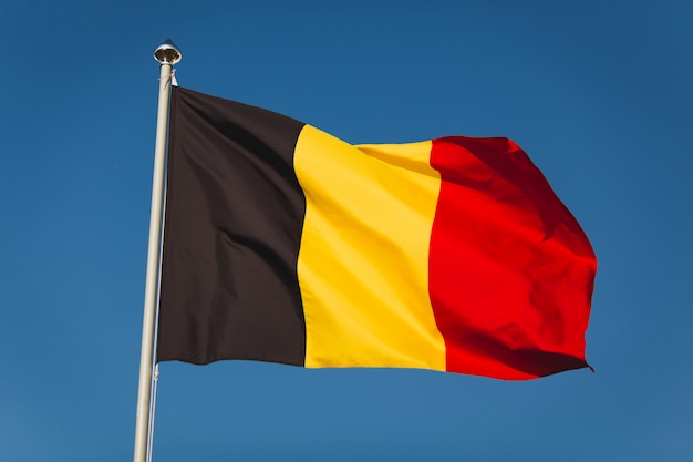 Foto flagge von belgien am mast. staatsflagge gegen blauen himmel des winds. flagge von belgien, hauptstadt bruxelles