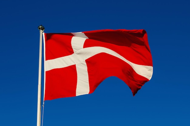 Flagge von Dänemark gegen den nationalen patriotischen Hintergrund des blauen Himmels