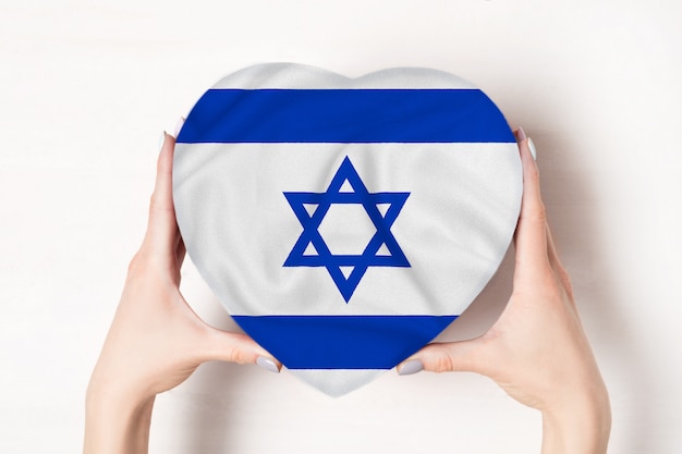 Flagge von Israel auf einem Herzen formte Kasten in weibliche Hände.