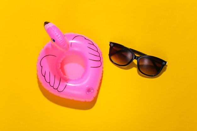 Flamenco rosado inflable con gafas de sol sobre fondo amarillo soleado. Concepto de vacaciones de verano. Minimalismo. Vista superior.