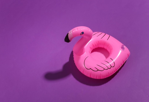 Flamingo rosa inflável sobre fundo roxo ensolarado. Conceito de férias de verão. Minimalismo