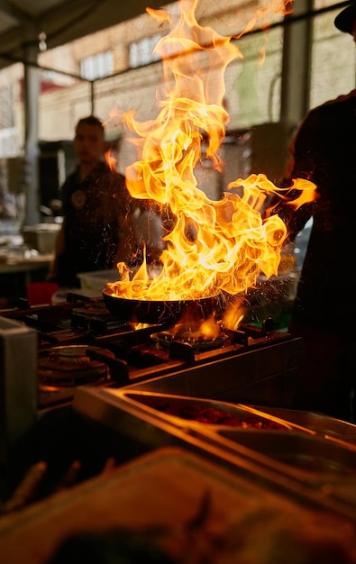 Flamme in der Pfanne Professioneller Koch macht Flamme für Speisen in der Restaurantküche