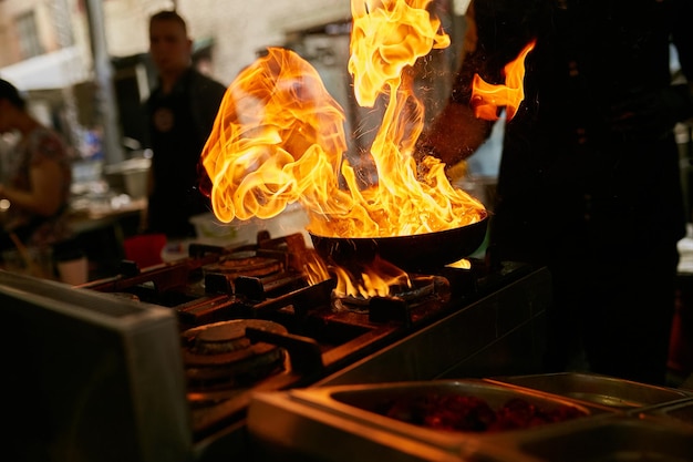 Flamme in der Pfanne Professioneller Koch macht Flamme für Speisen in der Restaurantküche