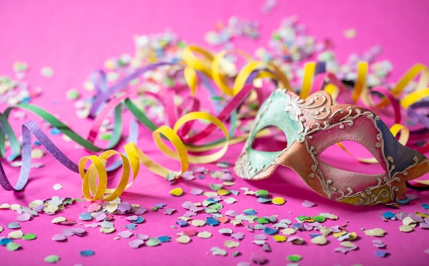 Foto flâmulas de máscara de carnaval e confetes em fundo rosa brilhante