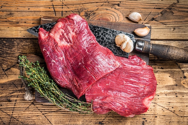 Flanquea los filetes de carne cruda sobre una tabla de cortar de carnicero con un cuchillo. fondo de madera. Vista superior.