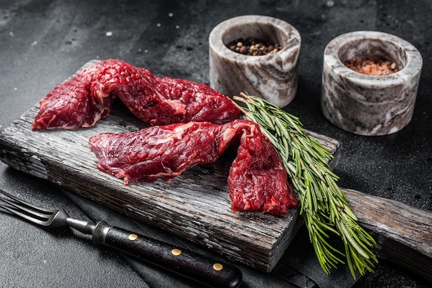 Flap steak flank raw cut y machete skirt steak sobre tabla de madera. Fondo negro. Vista superior.