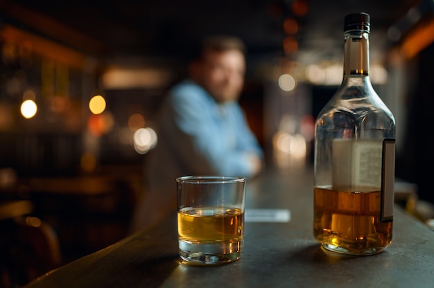 Flasche Alkohol und Glas auf der Theke in der Bar, männliche Person auf dlur-Hintergrund. Mann, der sich in der Kneipe ausruht, menschliche Emotionen und Freizeitaktivitäten, Stressabbaukonzept