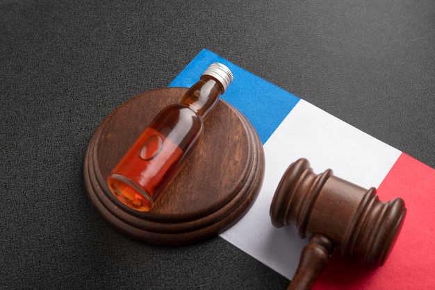 Flasche Alkohol und Holzhammer als Symbol des Gesetzes auf dem Hintergrund der französischen Flagge Alkoholgesetzgebung in Frankreich
